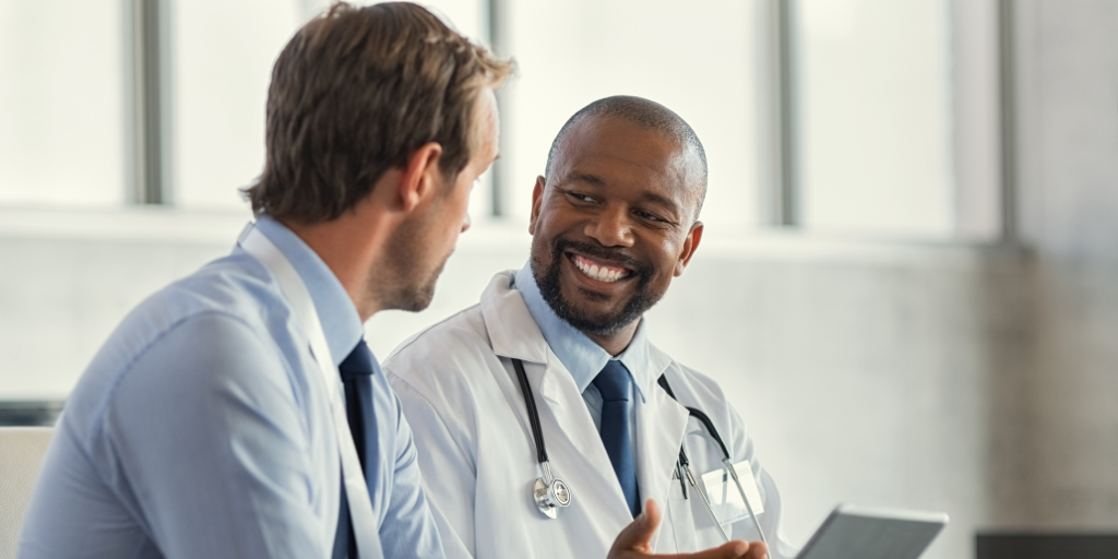 Male physician talking to another male while using tablet